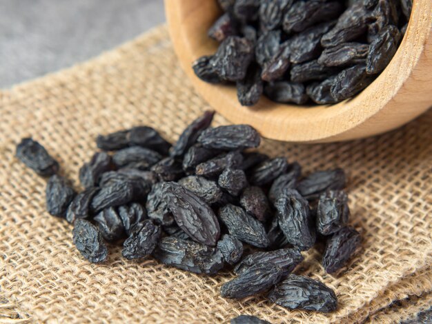 Dark raisins in a bowl on a dark concrete background