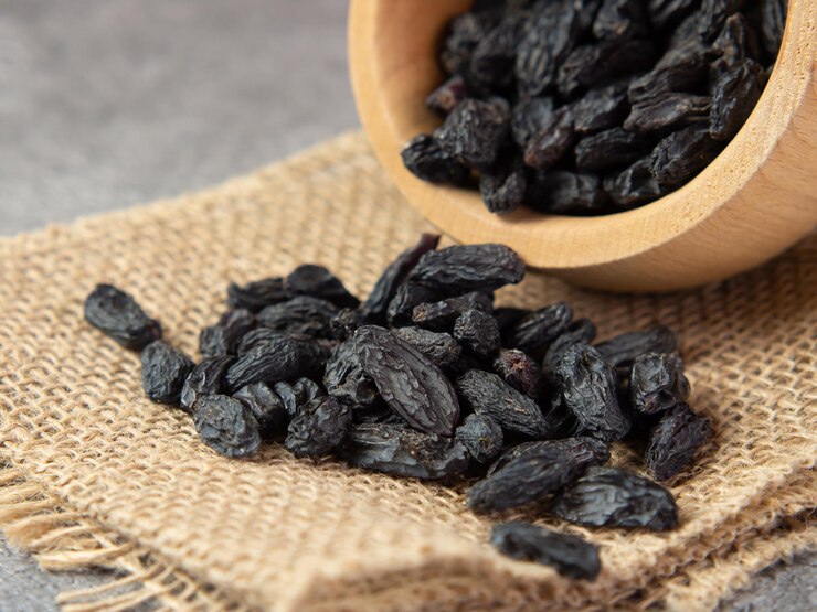 Dark raisins in a bowl on a dark concrete background