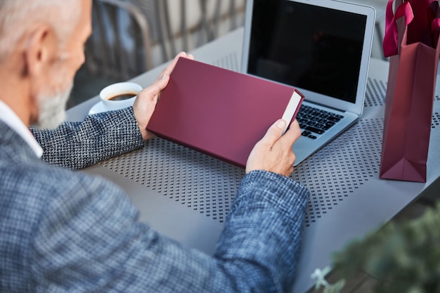 dark-red gift box in hands of a man sitting at a table with a laptop