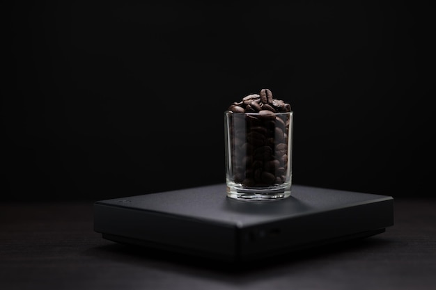 Dark roasted coffee beans in a clear glass on a black digital scale