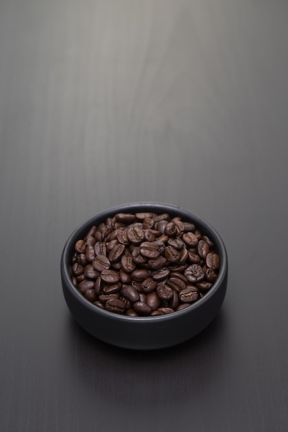 Dark roasted coffee beans in a small black ceramic bowl