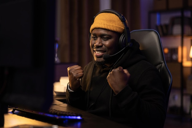 Dark room lit by led lights man sitting in front of computer wearing sweatshirt and yellow cap heads