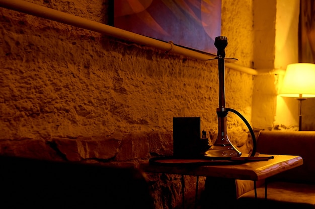 Dark room with working floor lamp, and black hookah on the table. High quality photo