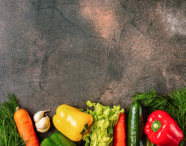 Dark rustic background with a border of fresh vegetables. top view.