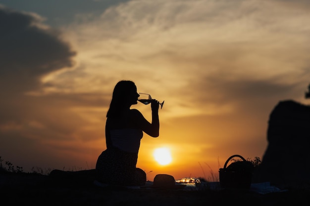 Dark silhouette of girl having a picnic and drinking a glass of champagne