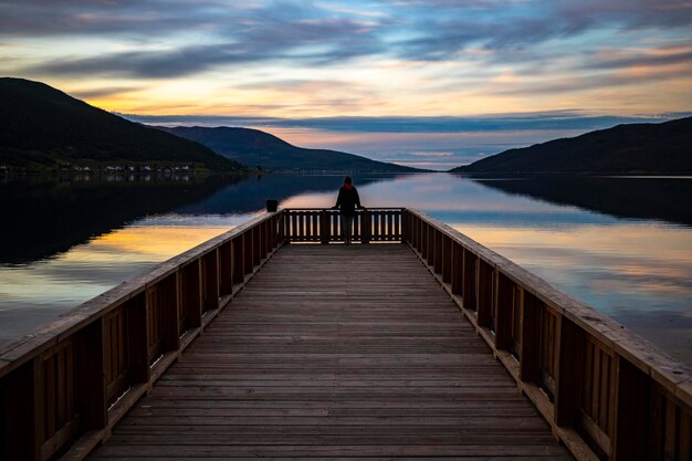 dark silhouette of a girl standing on a pier over the sea with a reflection of a colourful sunset