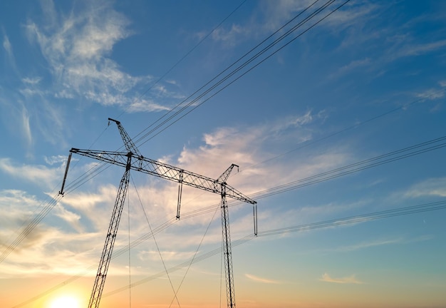 Dark silhouette of high voltage tower with electric power lines at sunrise Transmission of electric energy concept