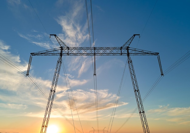 Dark silhouette of high voltage tower with electric power lines\
at sunrise transmission of electric energy concept
