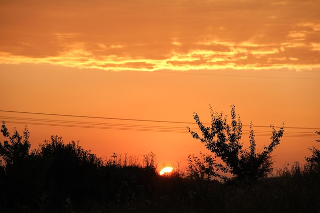 Dark silhouette of high voltage towers with electric power lines at sunrise