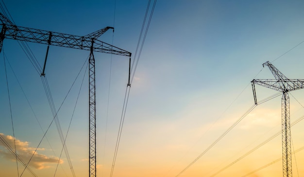 Dark silhouette of high voltage towers with electric power\
lines at sunrise