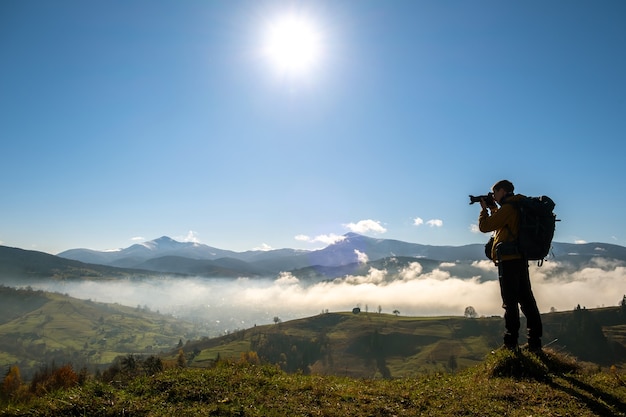 Dark silhouette of a hiker photographer taking picture of morning landscape in autumn mountains.