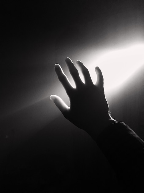 Dark silhouette of human hand in spotlight or backlight light with gesture with projector ray 