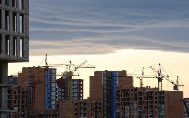 Dark silhouette of tower cranes at high residential apartment buildings construction site at sunset Real estate development