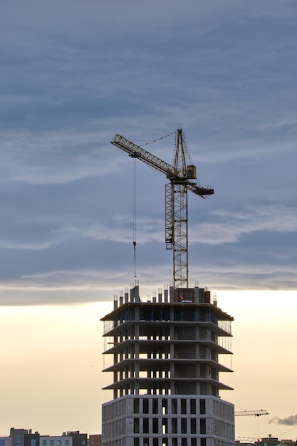 Dark silhouette of tower cranes at high residential apartment buildings construction site at sunset Real estate development