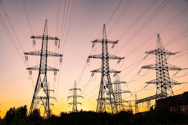 Dark silhouettes of electric towers on red sky background Transmission lines of highvoltage electric towers at sunset