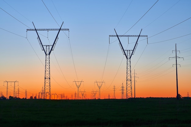 Dark silhouettes of power lines on fiery sunrise High voltage electricity towers in field and fiery sunset Concept of crisis of energy consumption generation and supply