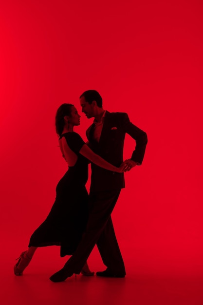 Dark silhouettes of tango dancers couple on red background