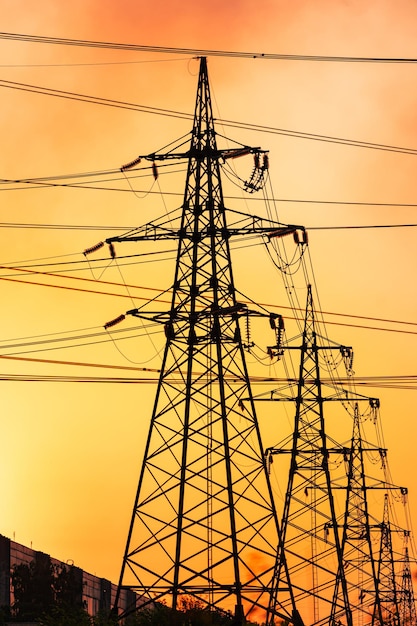 Dark silhouettes of transmission lines standing one by one in a row Power lines against the backdrop of setting sun Pink and yellow sky crossed by the power wires