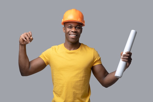 A dark-skinned construction engineer in a protective hemlet looking confident