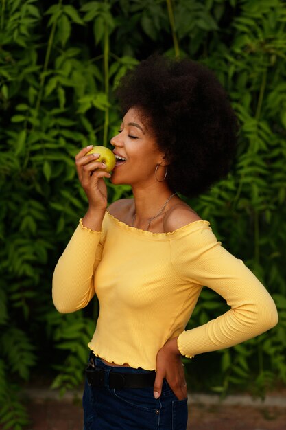 Dark-skinned girl has a green apple in the summer in the park