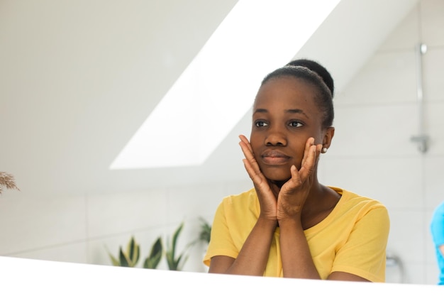 Dark skinned girl looking into mirror touching cheeks