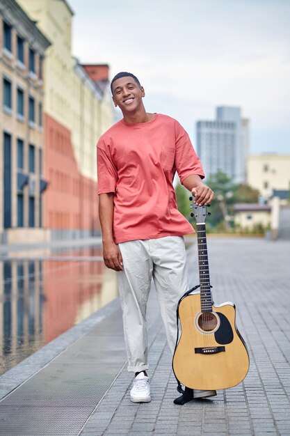 Dark-skinned man looking at camera standing with guitar