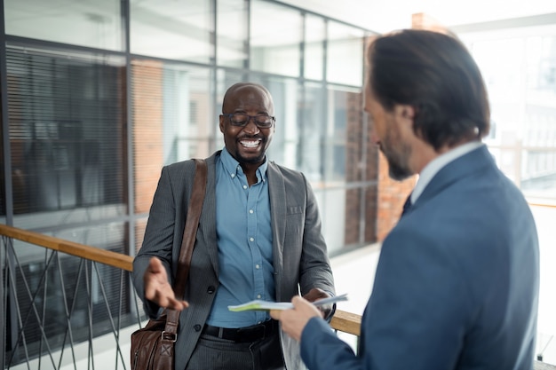 Dark-skinned man smiling. Cheerful dark-skinned man smiling while talking to business partner in the office