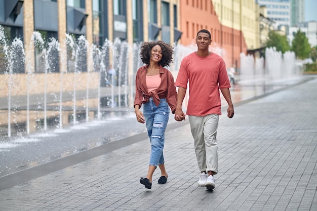 Photo dark-skinned man and woman holding hand walking