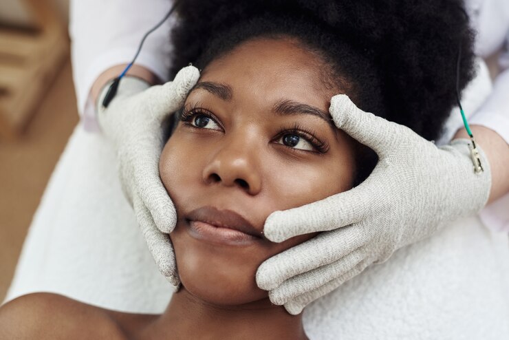 A dark-skinned model lies on the couch at the beautician and receives a microcurrent massage