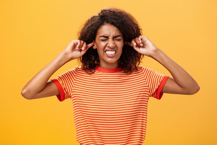 Photo dark skinned woman clenchign teeth and closing ears annoyed over orange wall