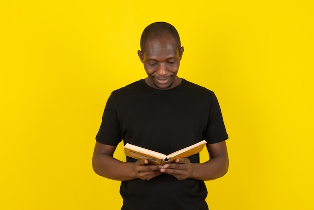 Dark-skinned young man reading interesting book on yellow wall