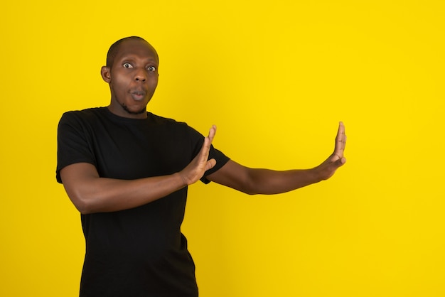 Photo dark-skinned young man staying away from something on yellow wall