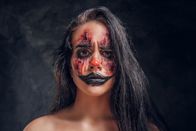 In the dark, smoky photo studio young girl has a photo shoot in a role of creepy clown.