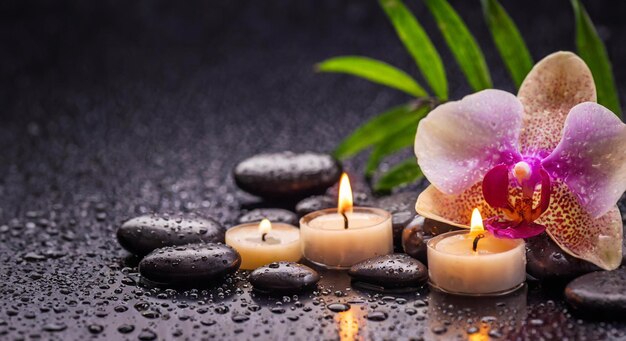 Dark spa background with massage stones candles pink orchid and drops of waters space for text