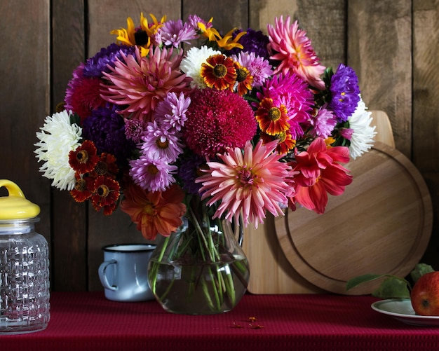 Dark still life with autumn flowers in a glass jug