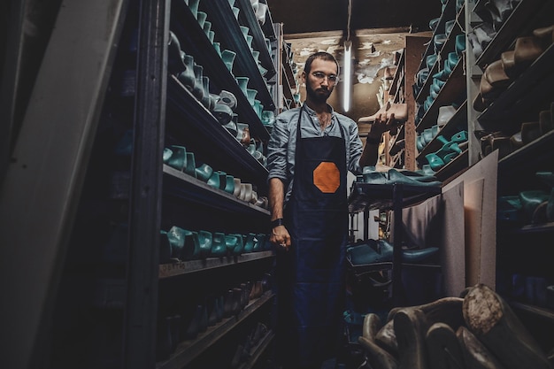 In the dark storage shoemaker in glasses is trying to find right shoe form.