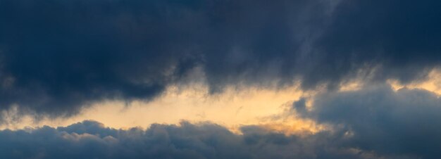 明るい夕陽のパノラマに照らされた暗い嵐の雲