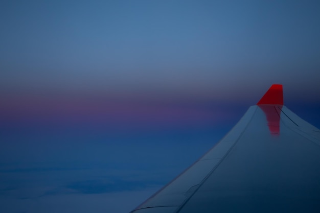 赤い翼を持つ飛行機の翼の下の暗い夕焼け空