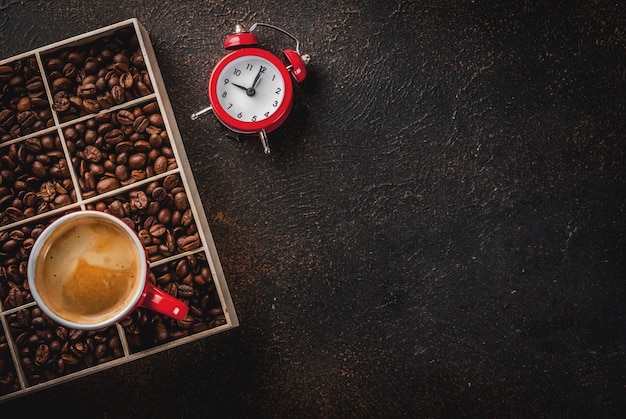 Dark surface with coffee beans, an alarm clock and a cup of coffee