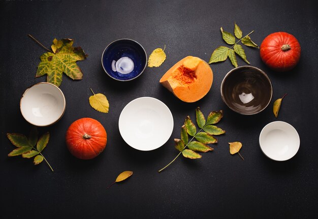 Dark table with empty plates and bowls  decorated with fresh whole pumpkins and fall yellow leaves composition. Autumn festive concept for Thanksgiving or Halloween celebration concept, top view