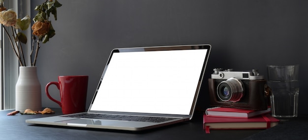 Dark trendy workspace with laptop computer and camera on black desk and dark grey wall 