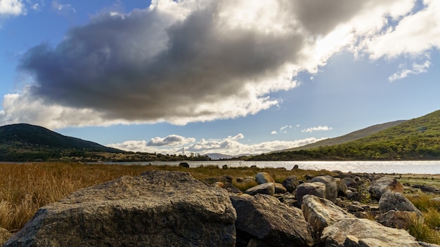 Dark winter landscape with fresh water lake, mountains on the horizon and dark clouds in the sky. Lozoya Reservoir, Madrid. Spain.