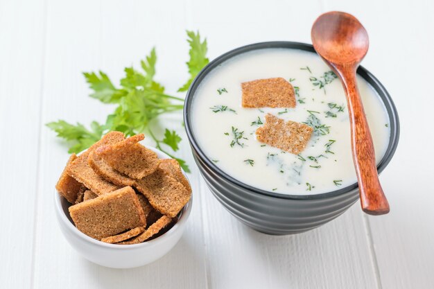 Dark wooden spoon on bowl with cream cauliflower soup on white table.