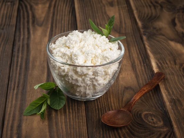 A dark wooden spoon next to a large bowl of fresh cottage cheese on a wooden table