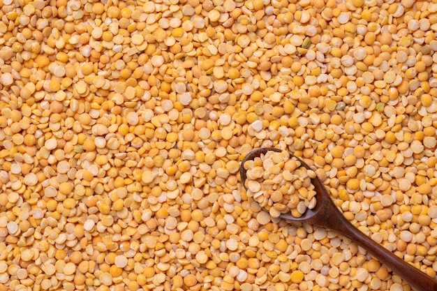 A dark wooden spoon lies on dry yellow peas. Top view, copy-space