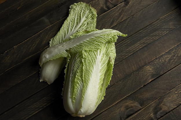 On a dark wooden table is a head of Peking cabbage with green leaves.