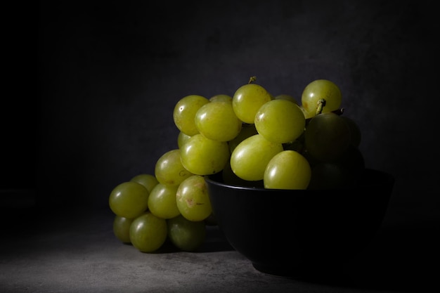 Darkfood style scene with a bunch of green grapes in a black compotera