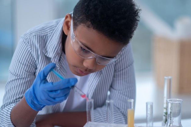 Un ragazzo dai capelli scuri con un camice da laboratorio che tiene una siringa con un reagente e sembra occupato