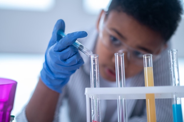 Un ragazzo dai capelli scuri con un camice da laboratorio che tiene una siringa con un reagente e sembra occupato