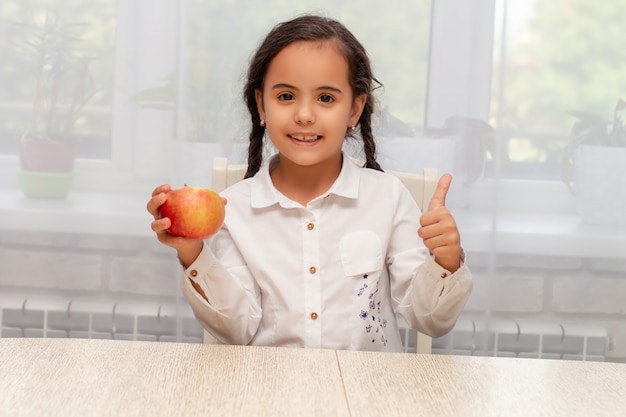 Photo a darkhaired girl with pigtails in a white shirt holds an apple in her hands